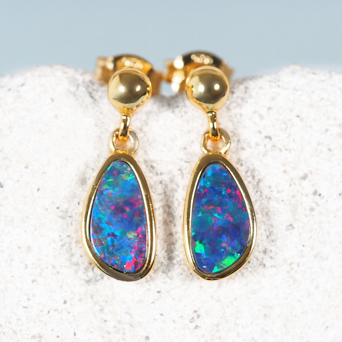 Gold opal earrings with colorful gemstones on a textured surface