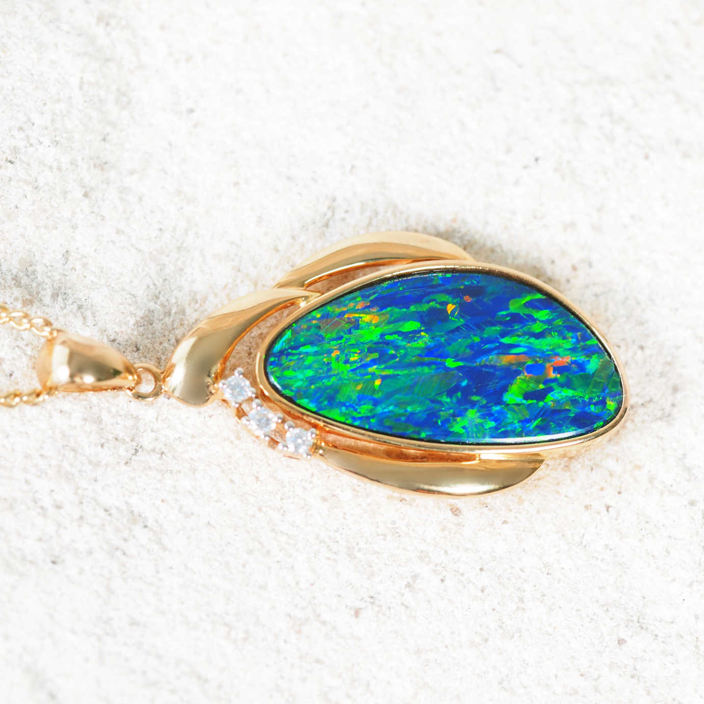 Teardrop opal pendant featuring vivid blue and green play-of-colour with three sparkling diamonds in yellow gold setting