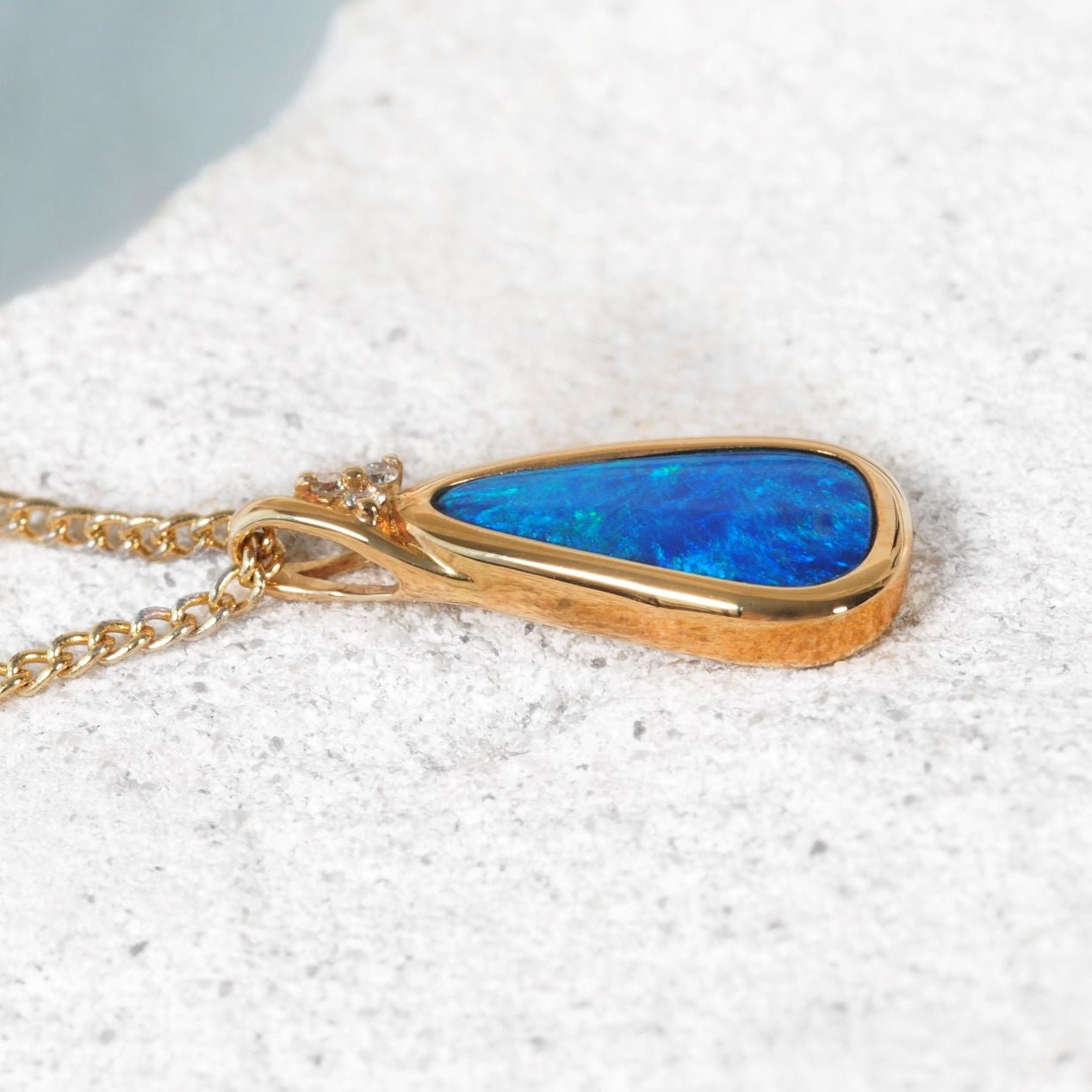 Gold necklace with a blue opal gemstone on a textured white surface