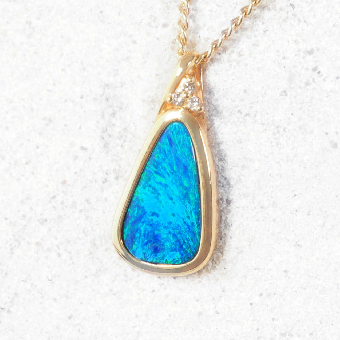 Elegant gold pendant with bezel-set Australian opal and trio of white diamonds.