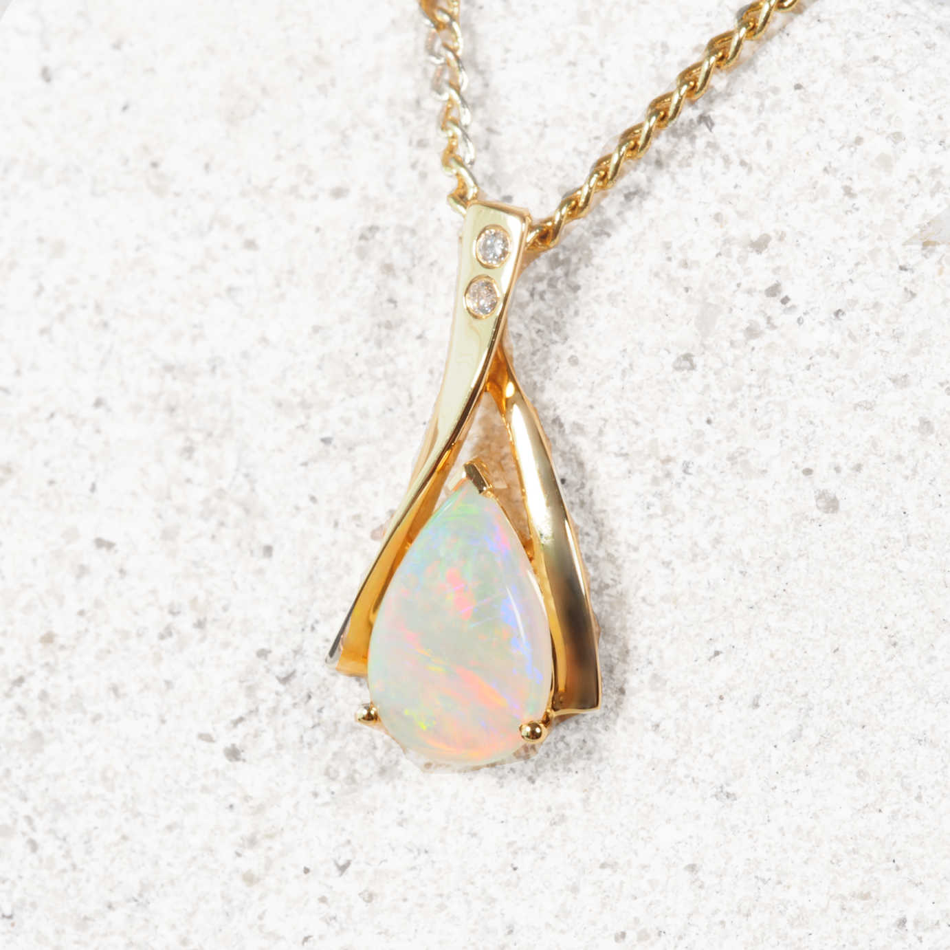 Gold pendant with a teardrop-shaped opal stone on a light background
