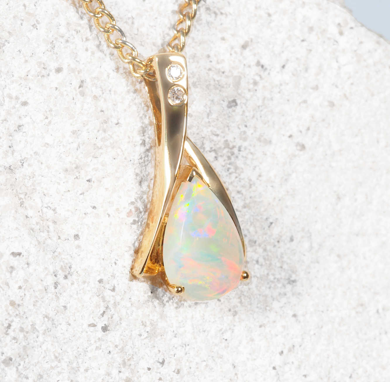 Gold pendant with a teardrop-shaped opal stone on a textured white surface