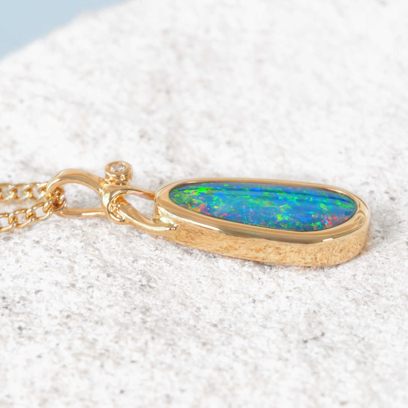 Gold necklace with a colorful opal pendant on a textured white surface