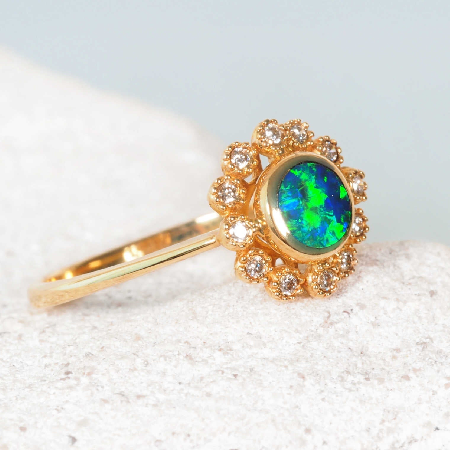 Gold ring with a green and blue opal stone on a light background