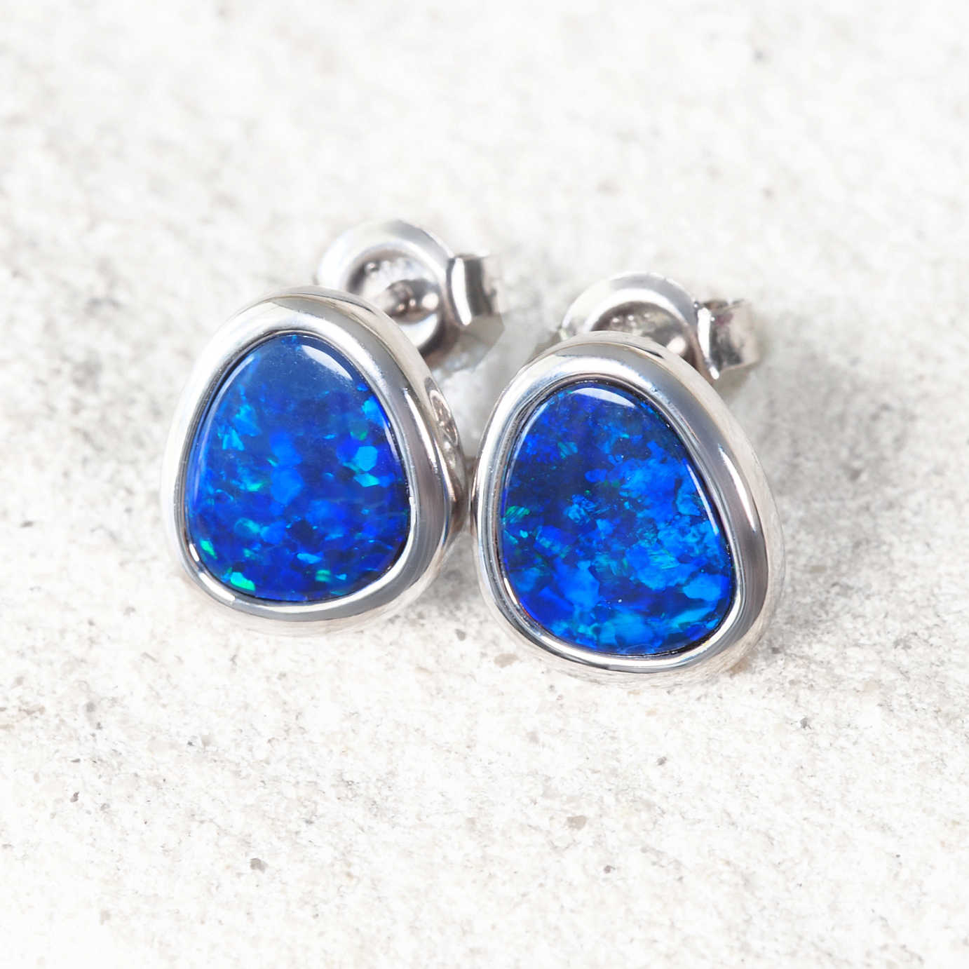 australian blue opal earrings set in white gold on a white rock