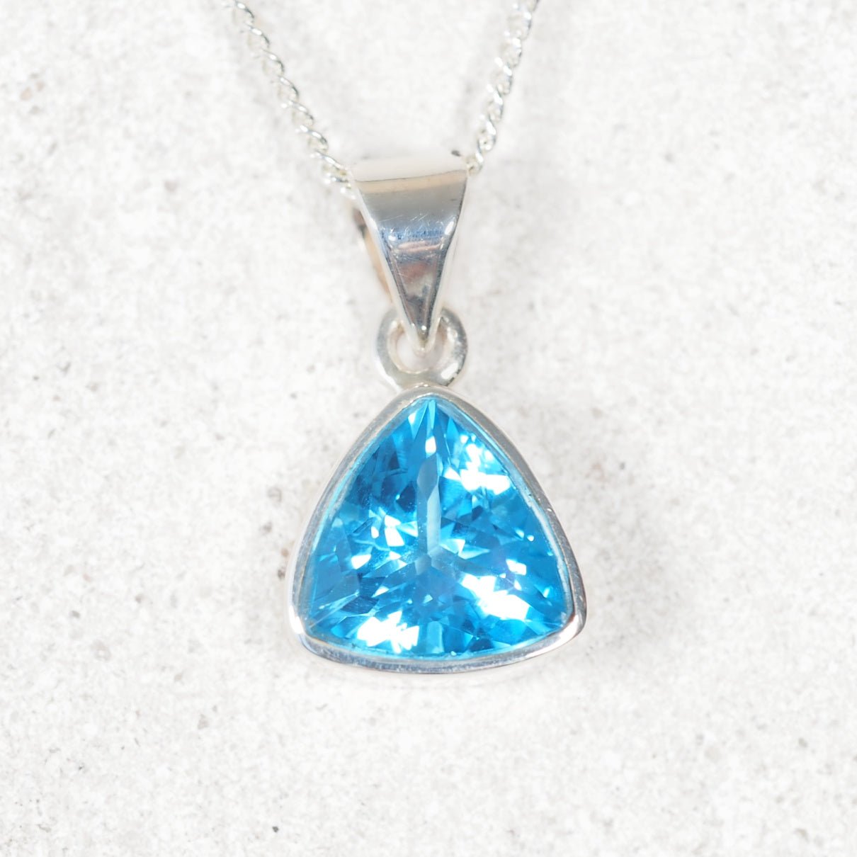 Blue topaz pendant displaying faceted triangular shape in a silver setting
