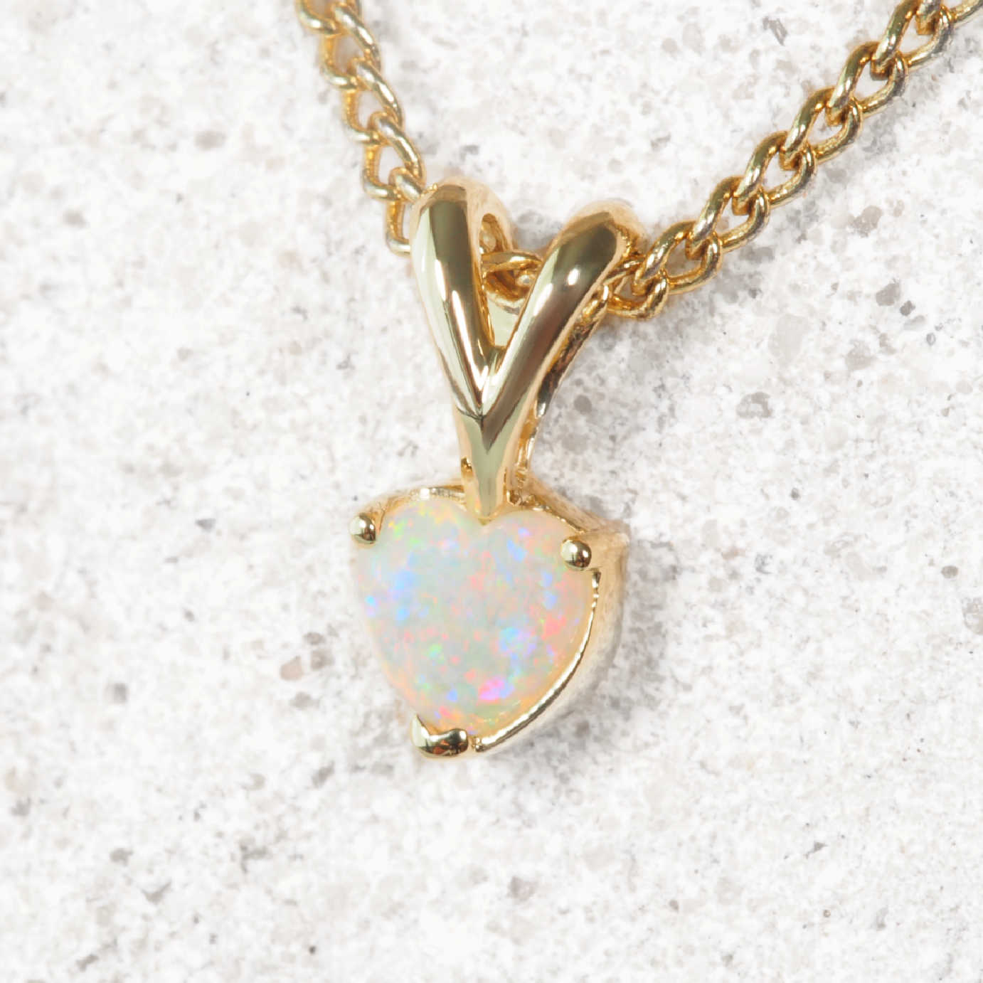 Gold necklace with a heart-shaped opal pendant on a light gray background