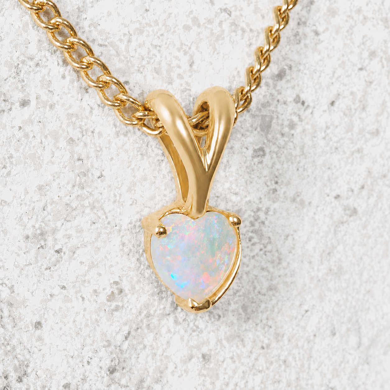 Gold necklace with a heart-shaped opal pendant on a textured white background