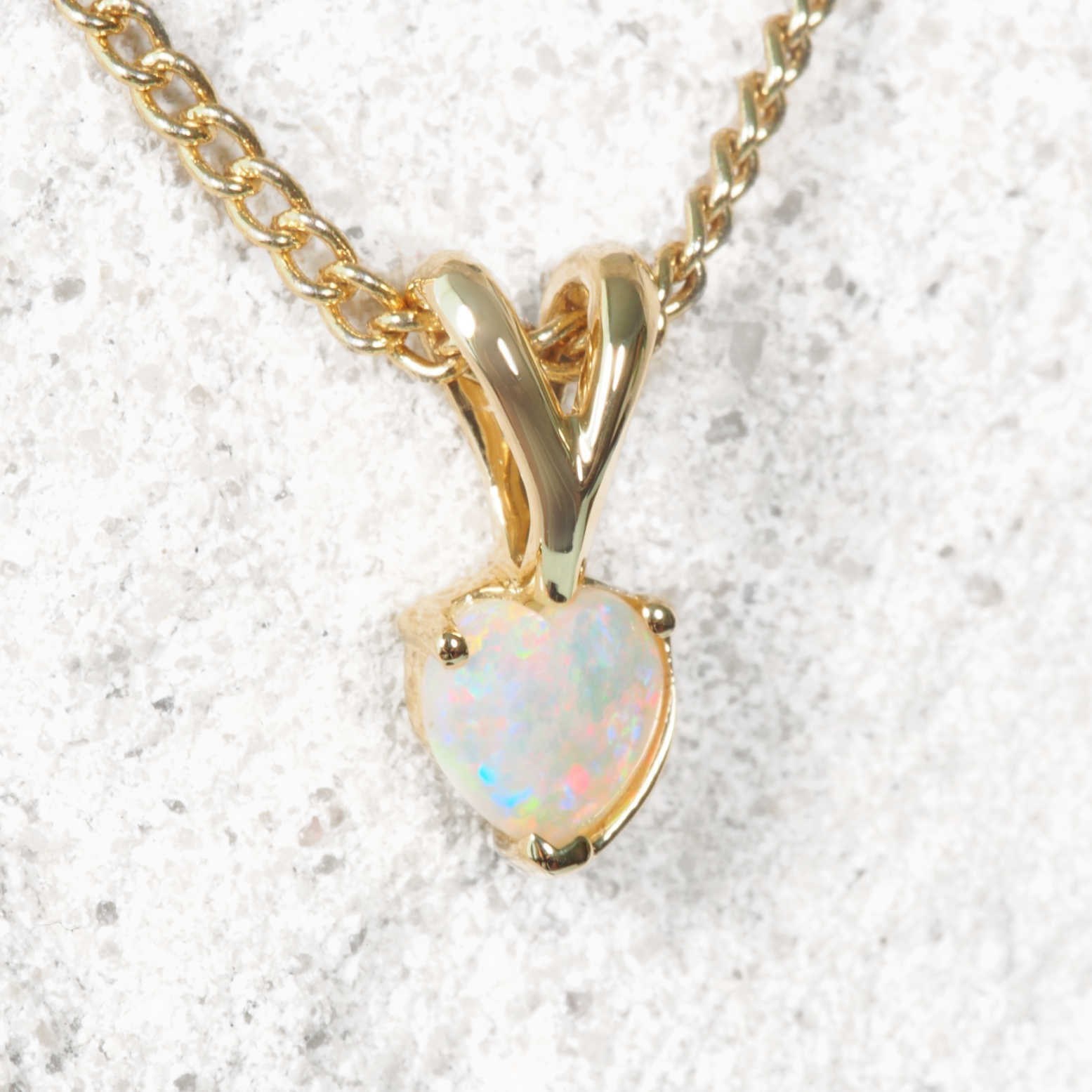 Gold necklace with a heart-shaped opal pendant on a textured white background