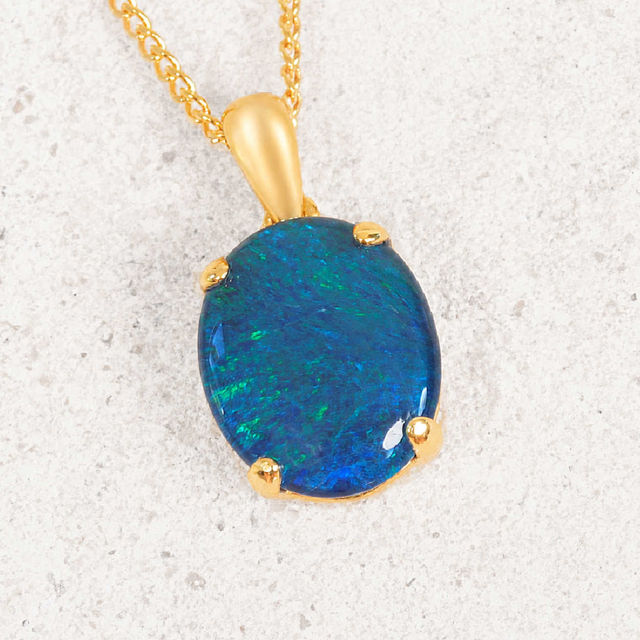 Gold pendant with a blue opal gemstone on a textured white background