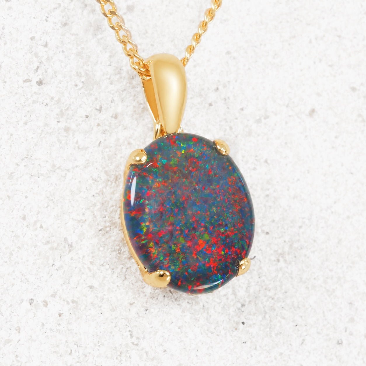Opal pendant necklace with gold setting on a textured white background