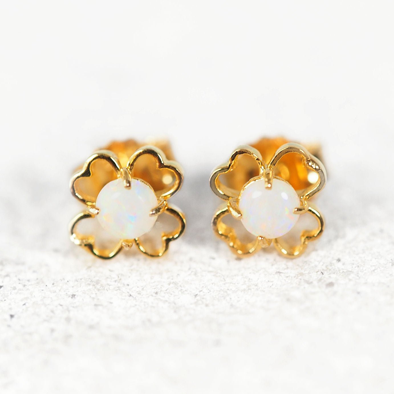 Gold flower-shaped opal earrings with white centers on a light background