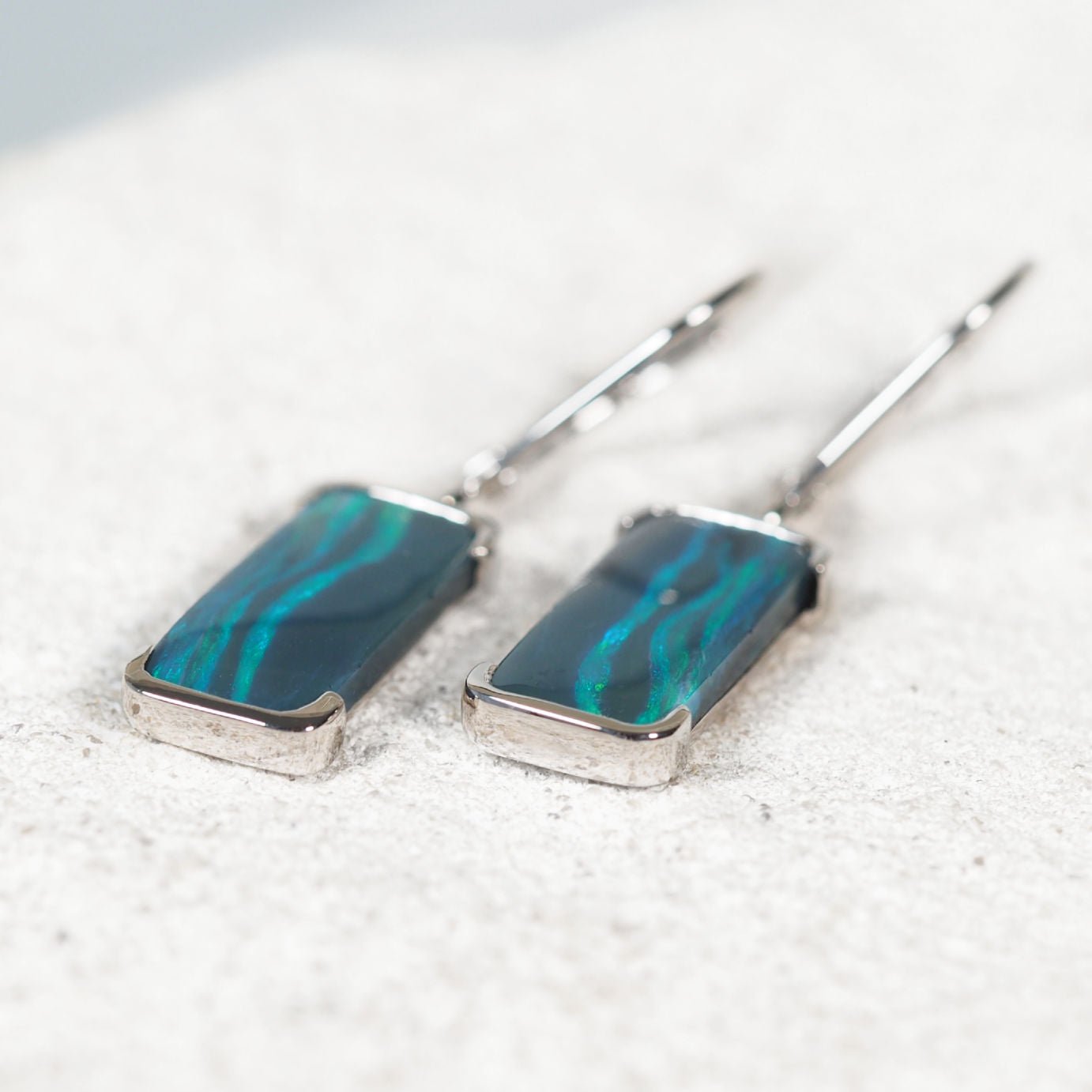 Close-up of 'Corinna' opal earrings showing bezel-set solid black opals glowing green in polished white gold