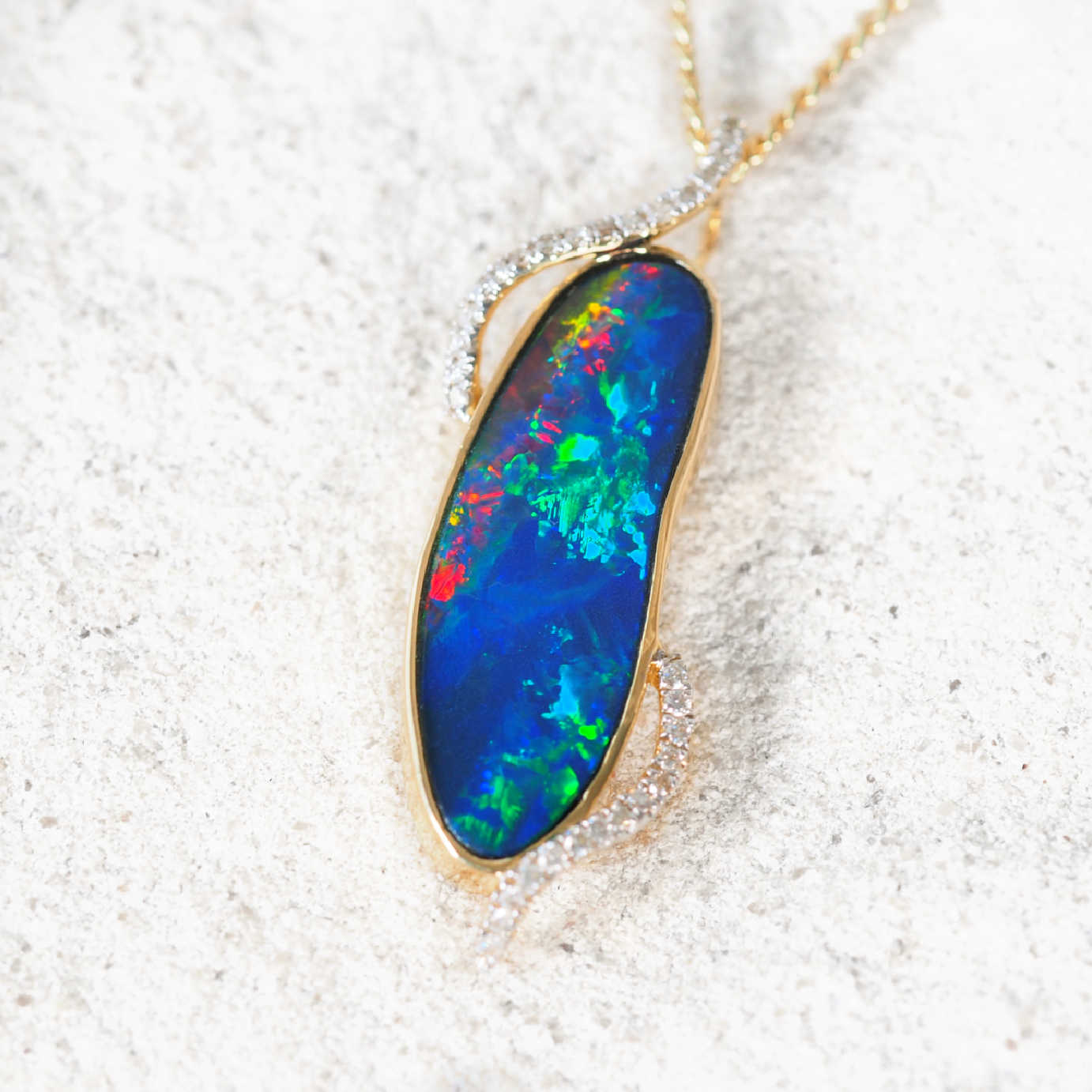 Close-up of Australian doublet opal pendant showing vibrant blue and green play-of-colour in yellow gold setting