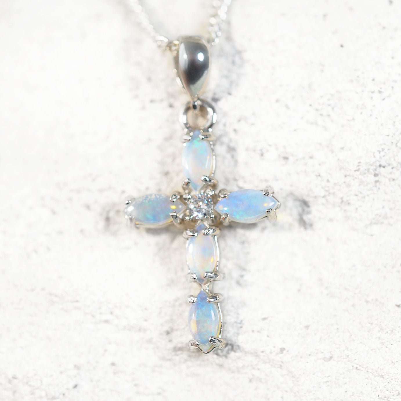 Blue Opal cross silver pendant on a white rock background