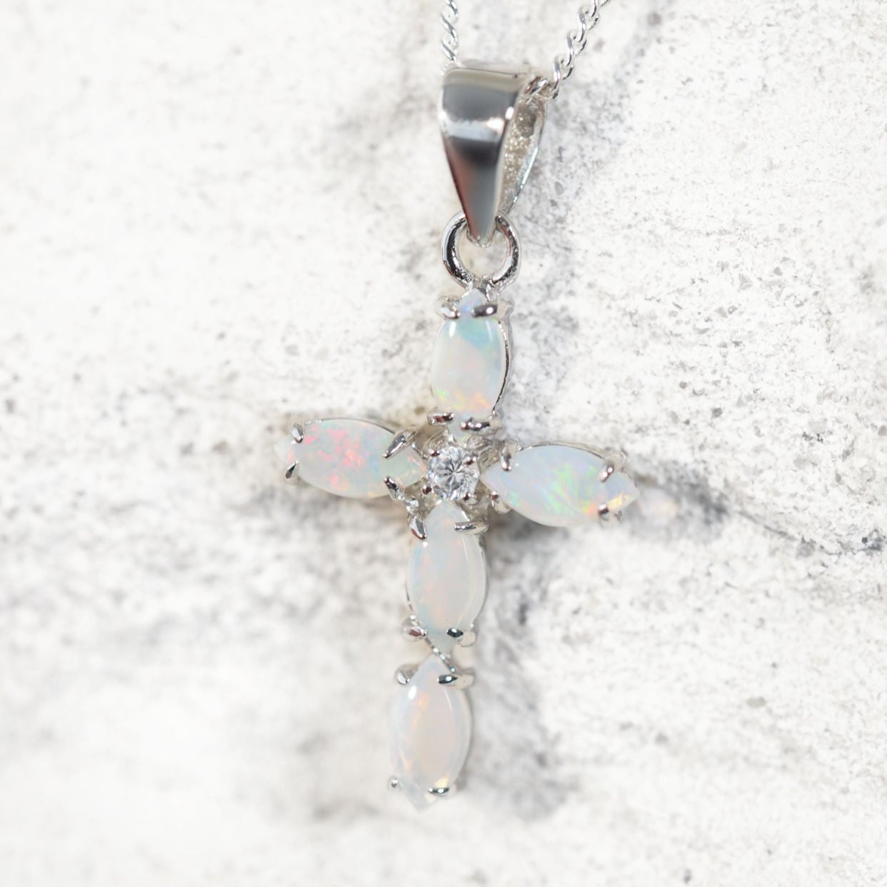Opal cross pendant on a chain against a light background