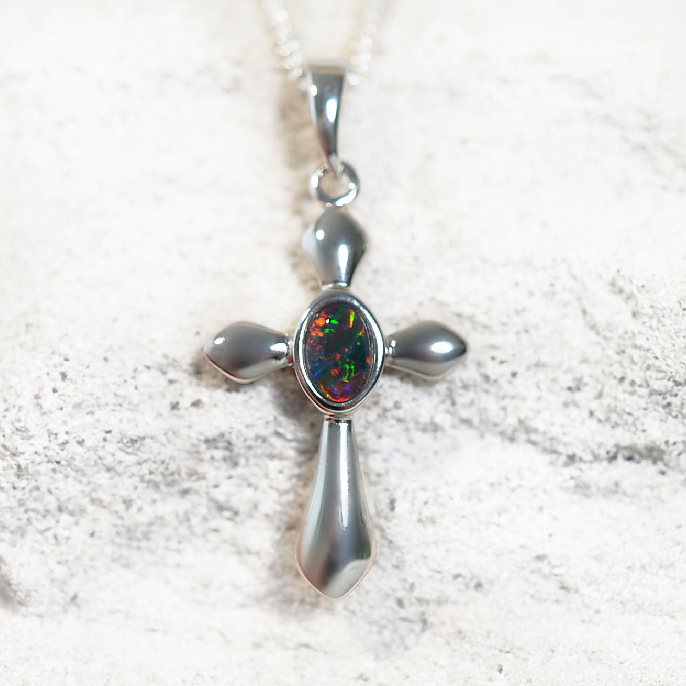 Silver cross opal pendant with a colorful gemstone on a textured white background
