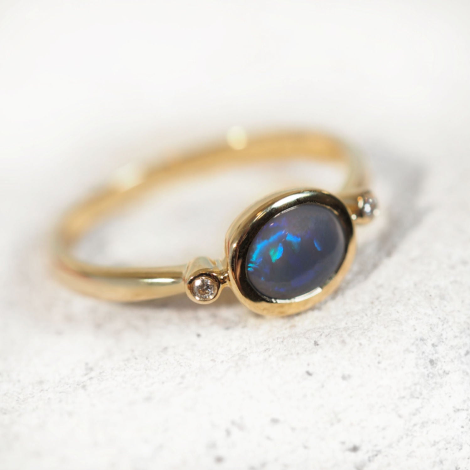 Elegant 14ct yellow gold opal ring featuring oval black crystal opal in blue-green hues with bezel-set diamond accents