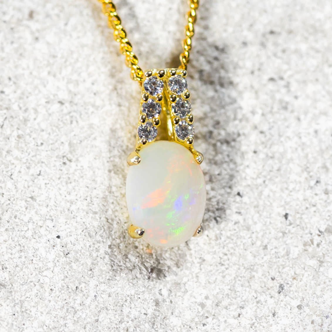 Opal gold plated silver pendant necklace with gold chain on a textured surface