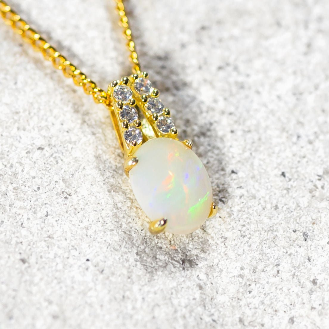 Opal pendant necklace with gold chain on a textured surface