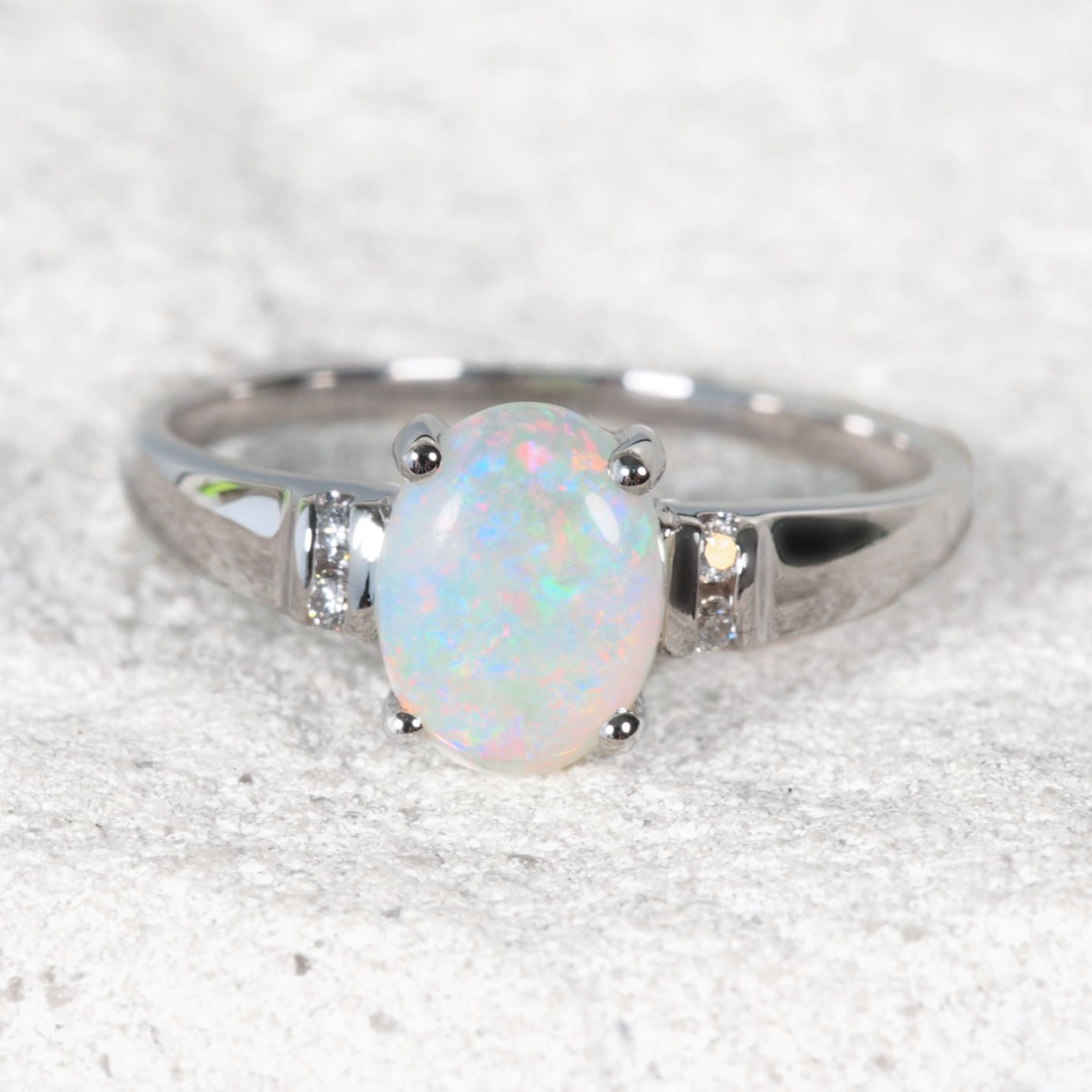 Colourful white opal ring with diamonds on a white rock