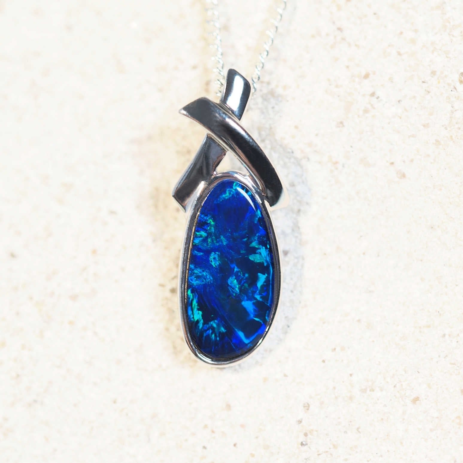 Elegant 14ct white gold opal necklace with blue-and-green oval-shaped Australian doublet opal in a contemporary cross design.