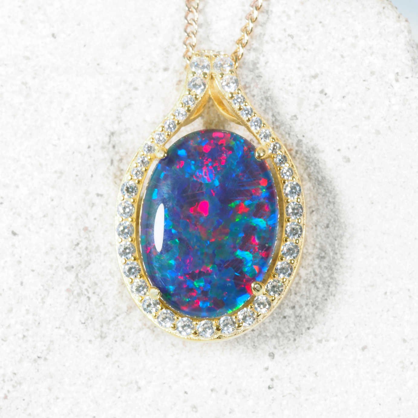 Opal pendant necklace with gold frame and gemstones on a white background