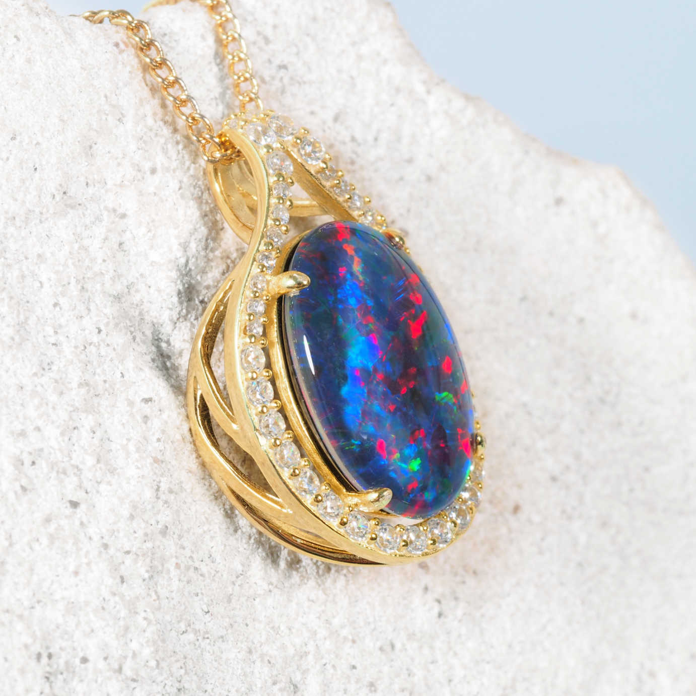 Opal pendant with gold plated silver setting on a textured white surface