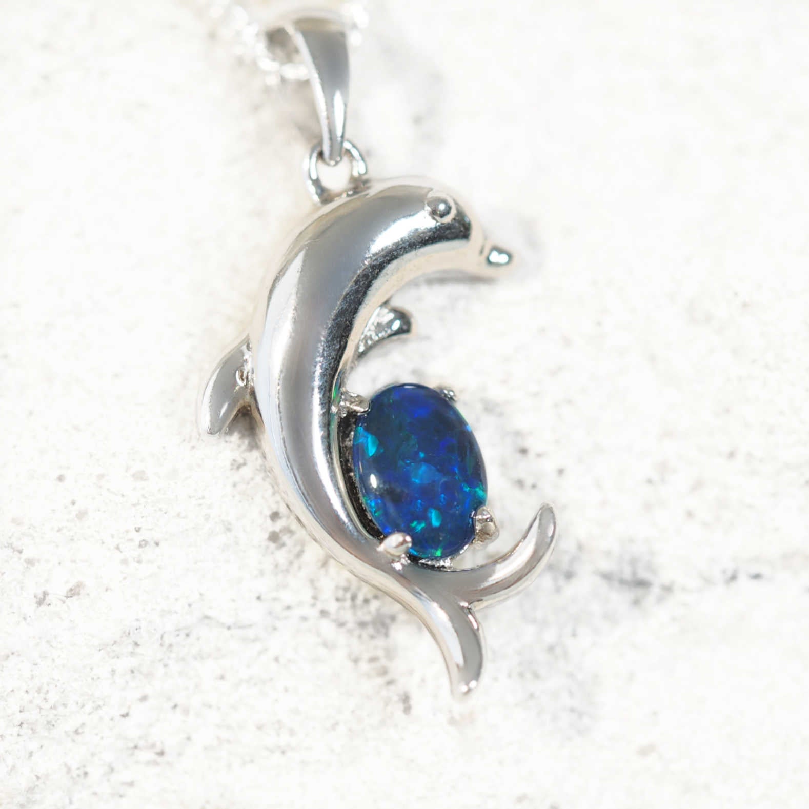Silver dolphin design opal pendant with a blue stone on a white background