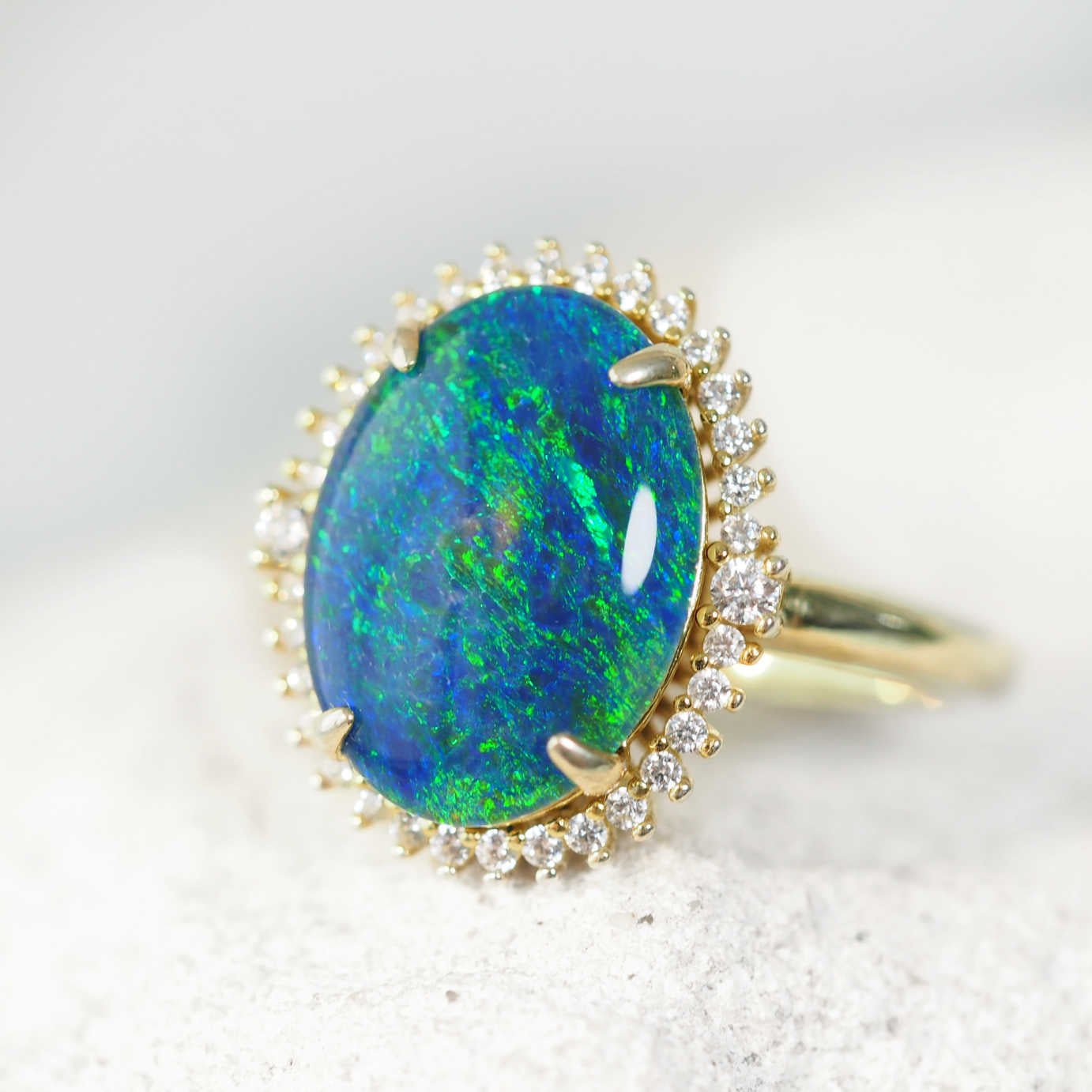 Ring with a blue and green opal stone and gold plated silver setting on a light background