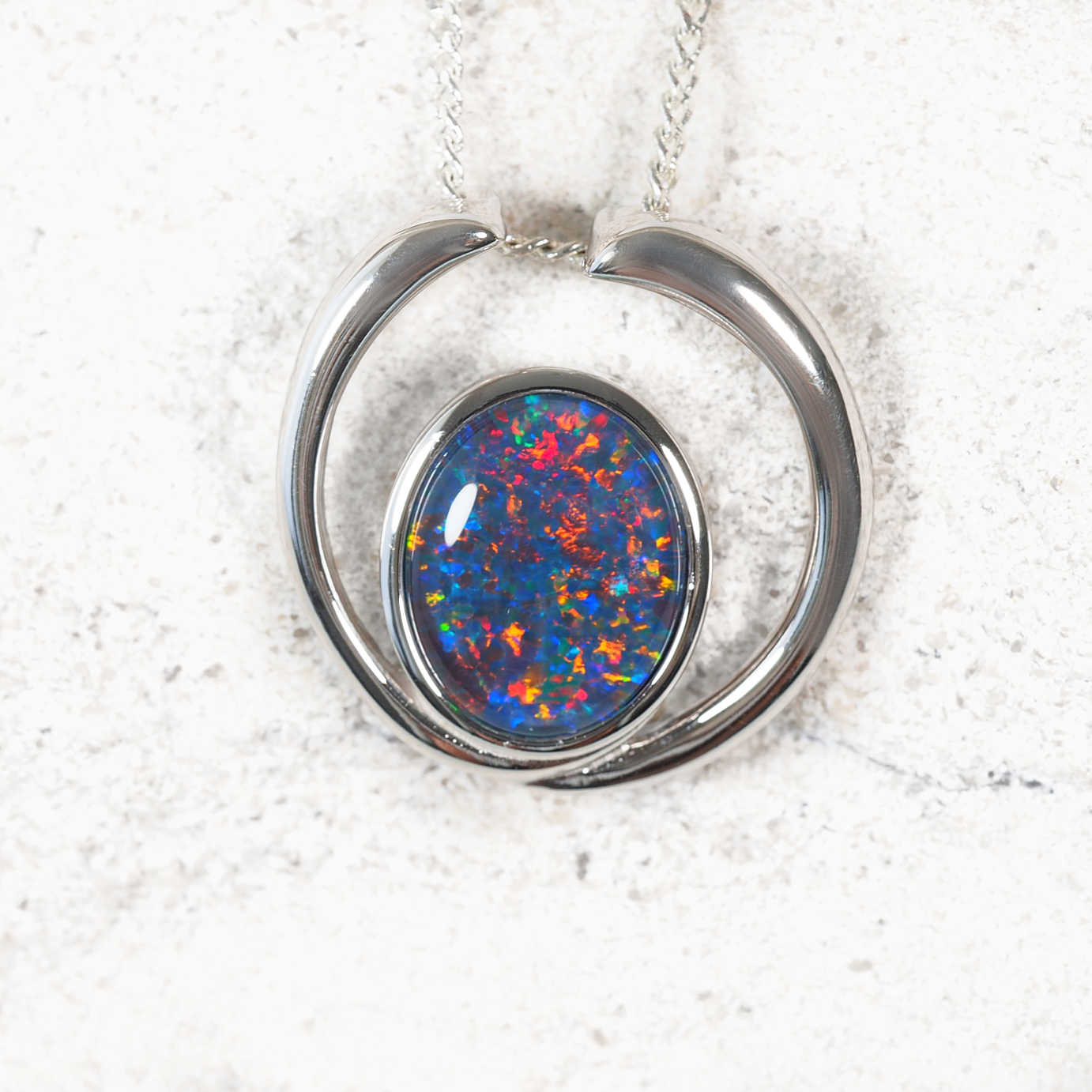 Necklace with a multicolored opal gemstone pendant on a textured white background