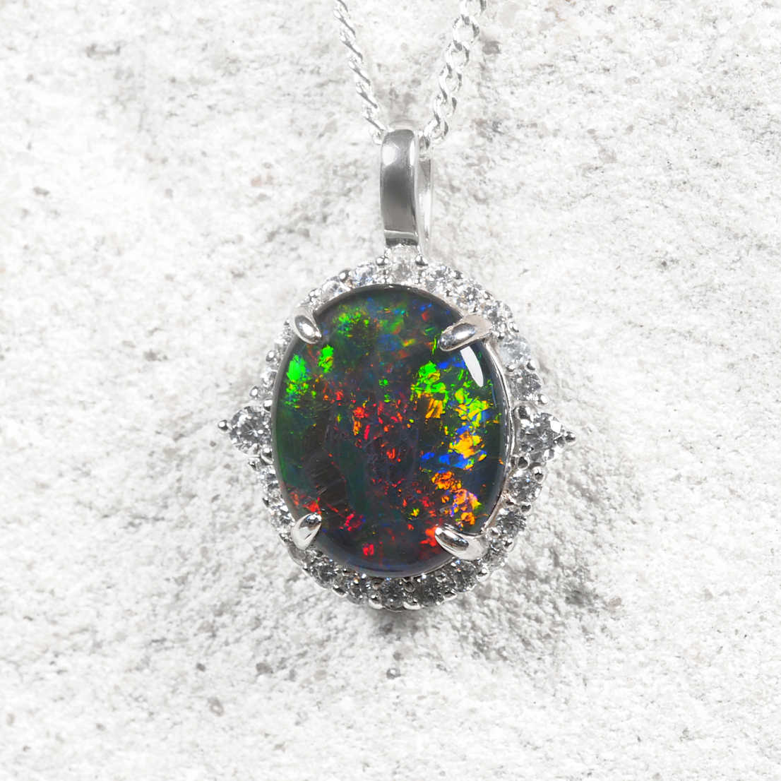 A Sterling silver Australian opal pendant featuring an oval triplet opal with vibrant red, green and blue play-of-colour, surrounded by sparkling cubic zirconias