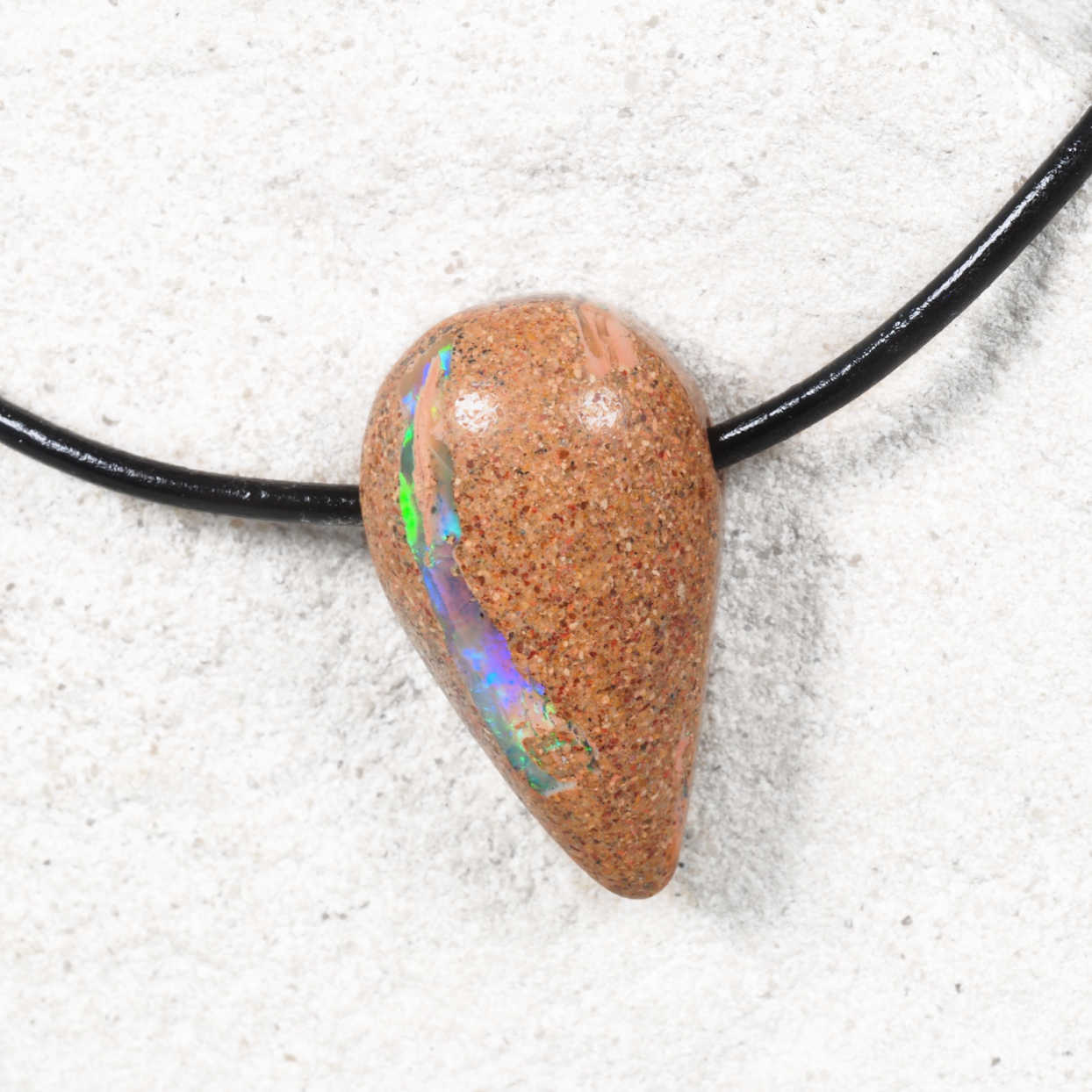 Opal pendant on a black cord against a sandy background