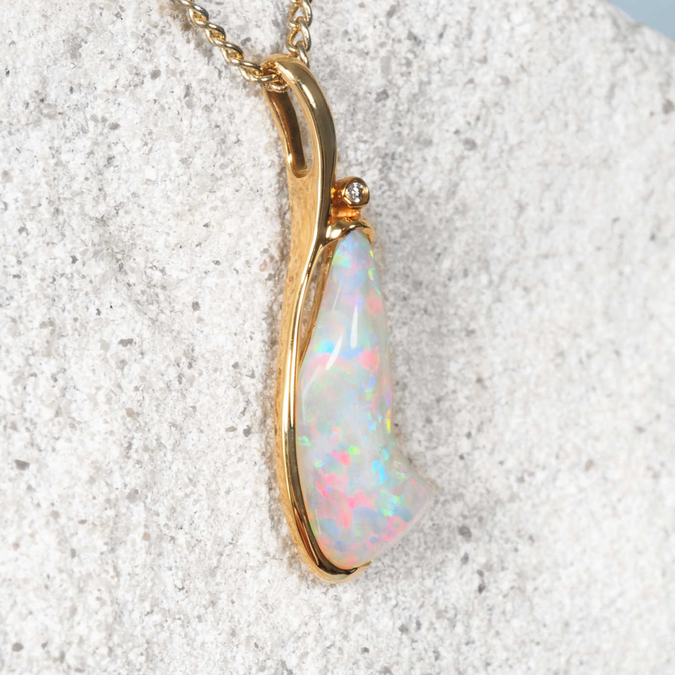White opal pendant with gold setting on a textured surface