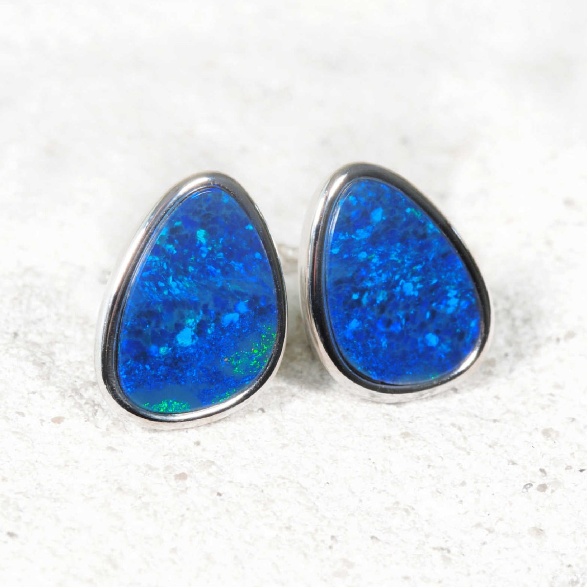 A pair of teardrop-shaped australian opal stud earrings featuring vibrant blue opal stones in silver bezel settings.
