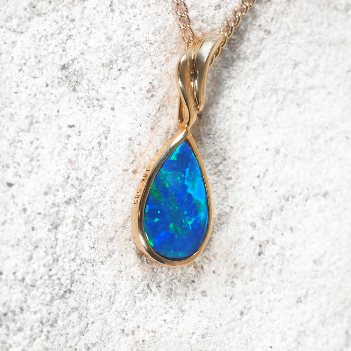 Gold pendant with a blue opal stone on a textured white background