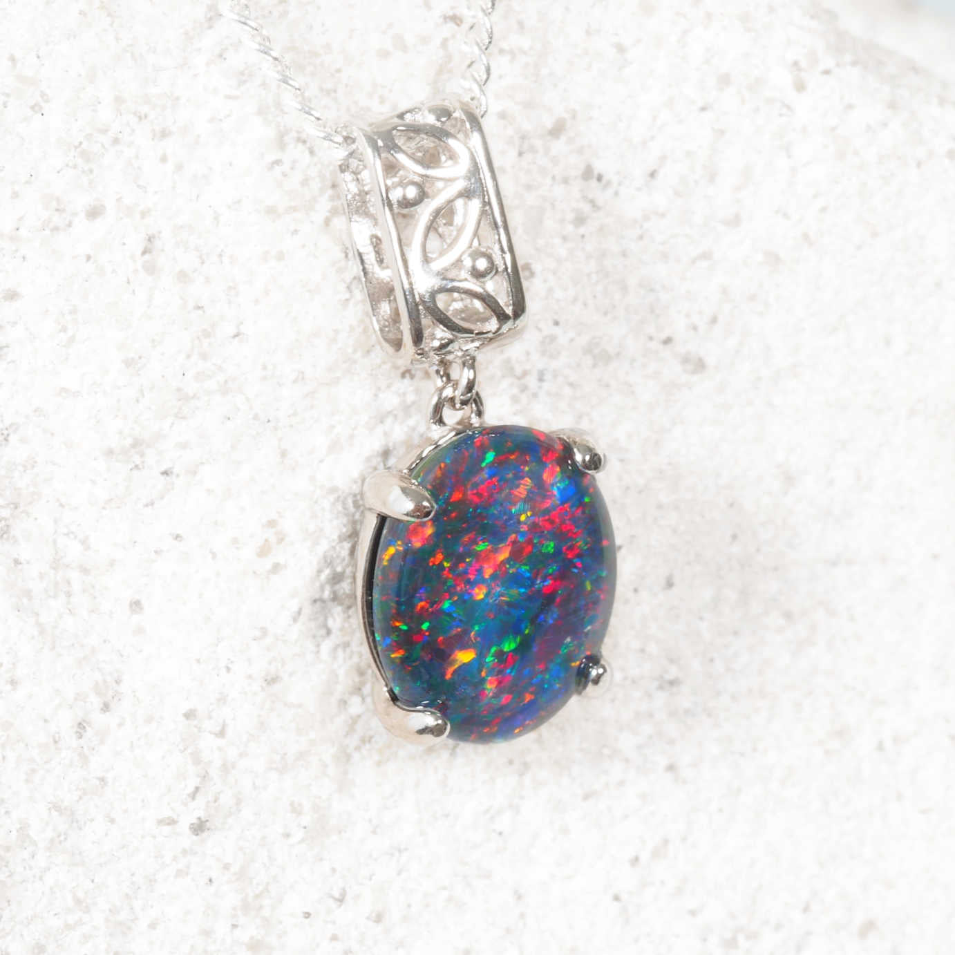 Triplet opal pendant with silver setting on a white rock background