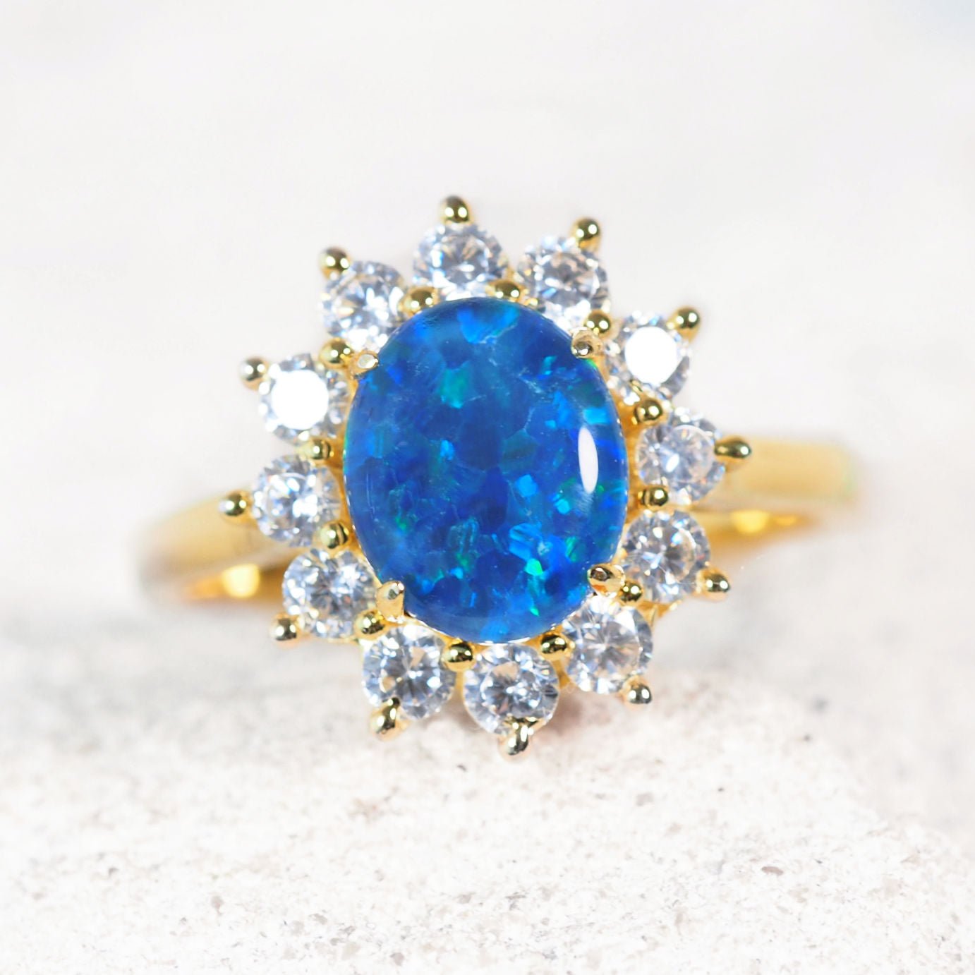 Gold ring with a blue opal gemstone and smaller diamonds on a light background