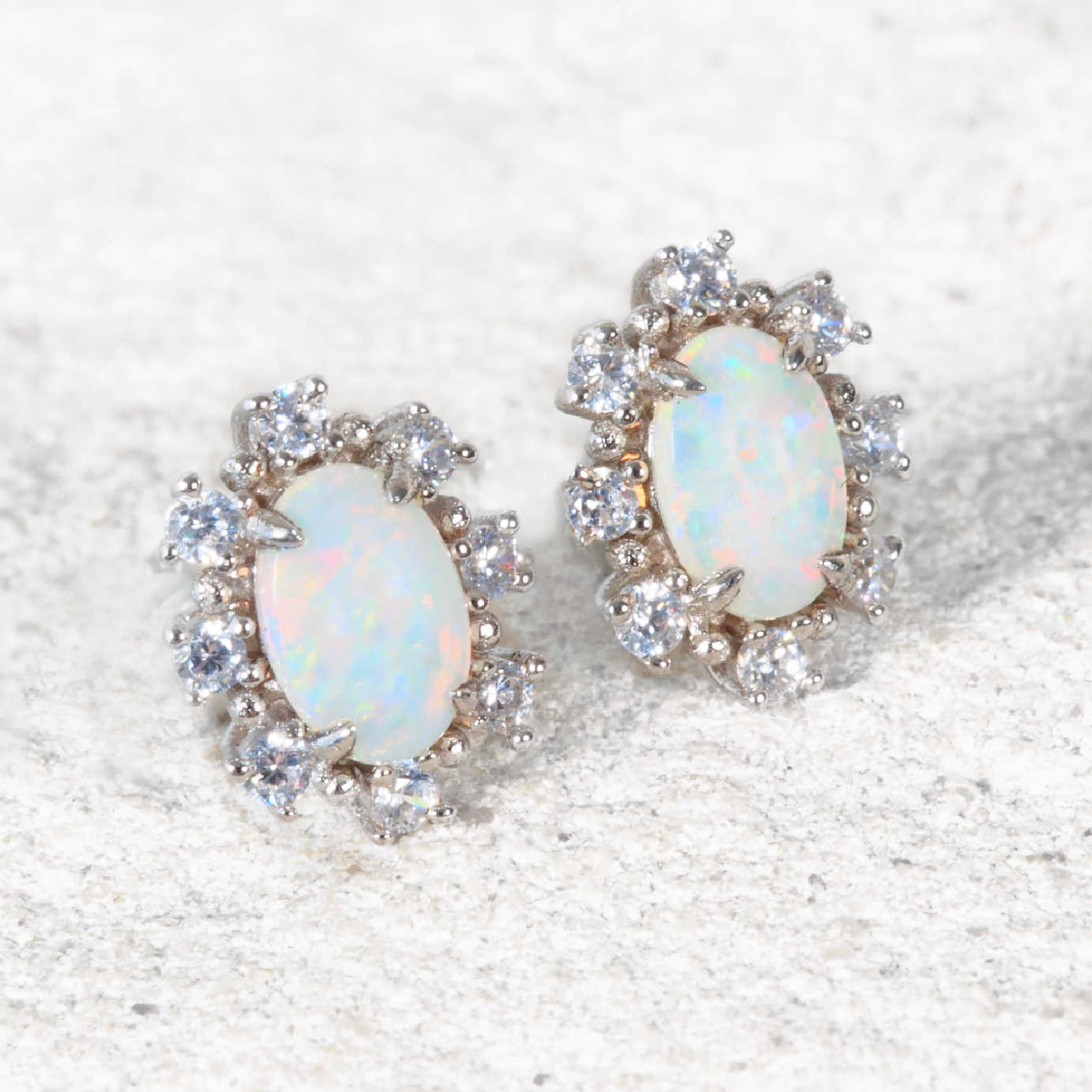 Pair of opal earrings with diamond accents on a textured white surface