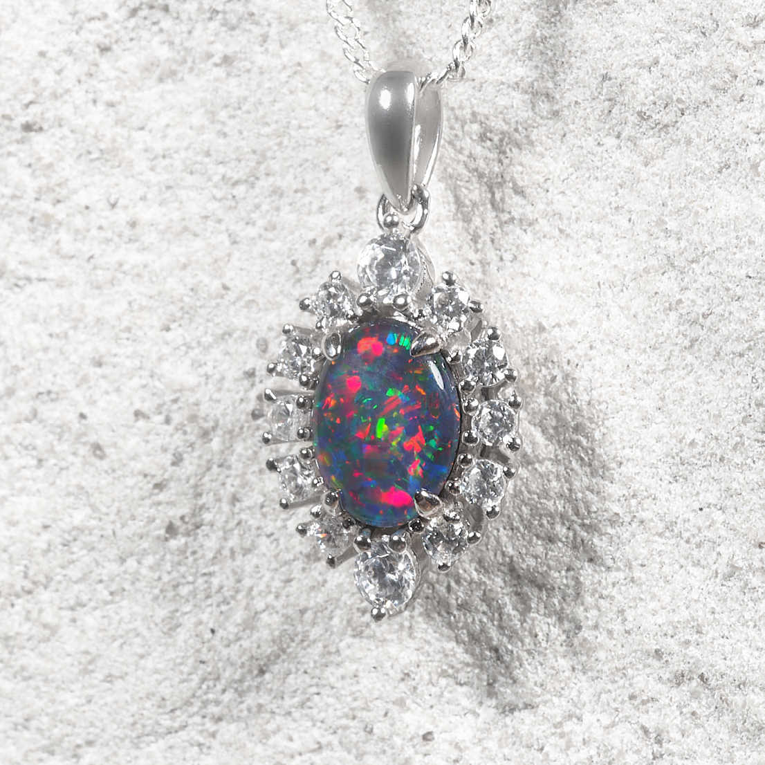 Oval Australian triplet opal pendant crafted in sterling silver with vivid natural play-of-colour and a sparkling twelve-stone cubic zirconia halo.