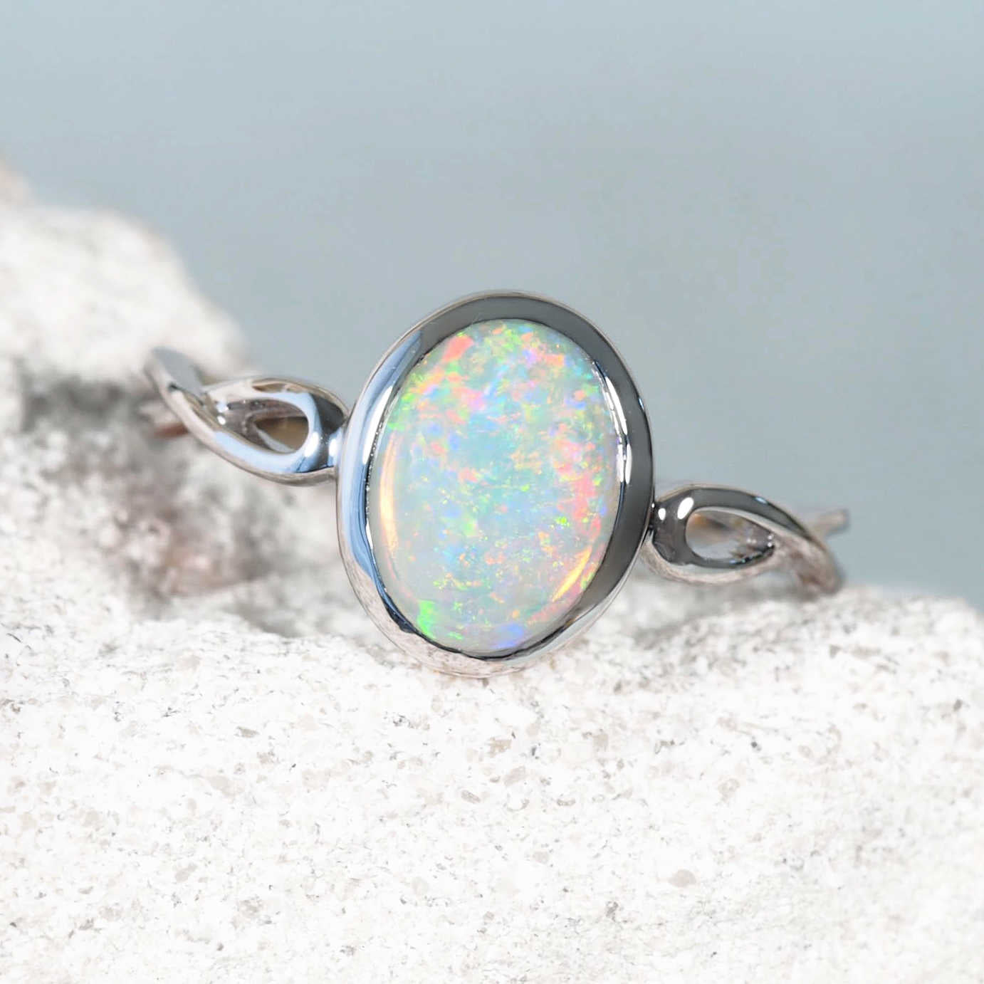 White gold ring set with a colorful opal stone on a light gray background
