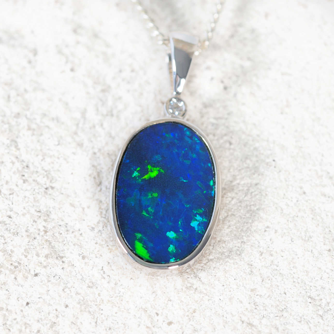 Oval Australian doublet opal pendant showing vivid blue and green play-of-colour in white gold setting
