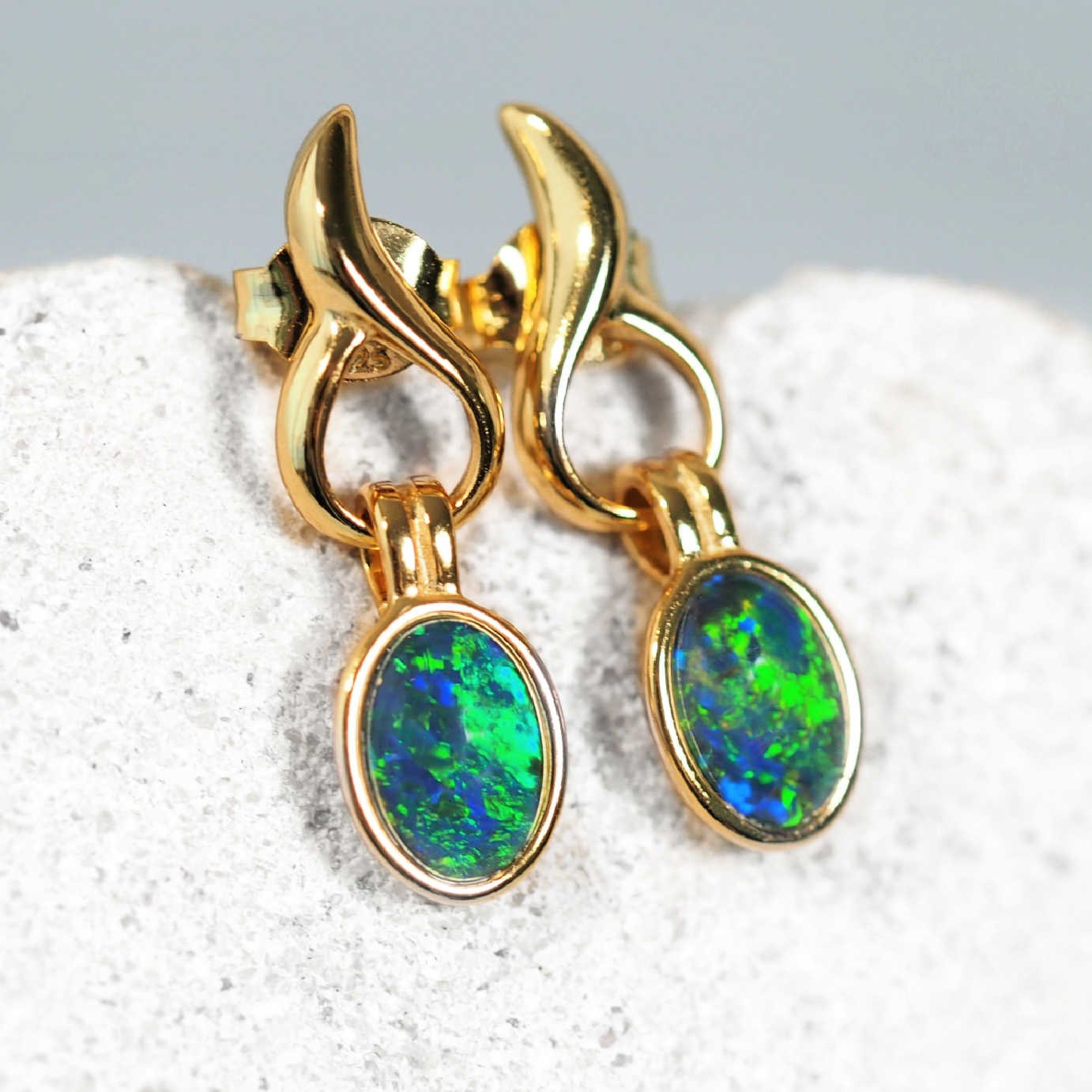 Gold earrings with opal stones on a textured surface
