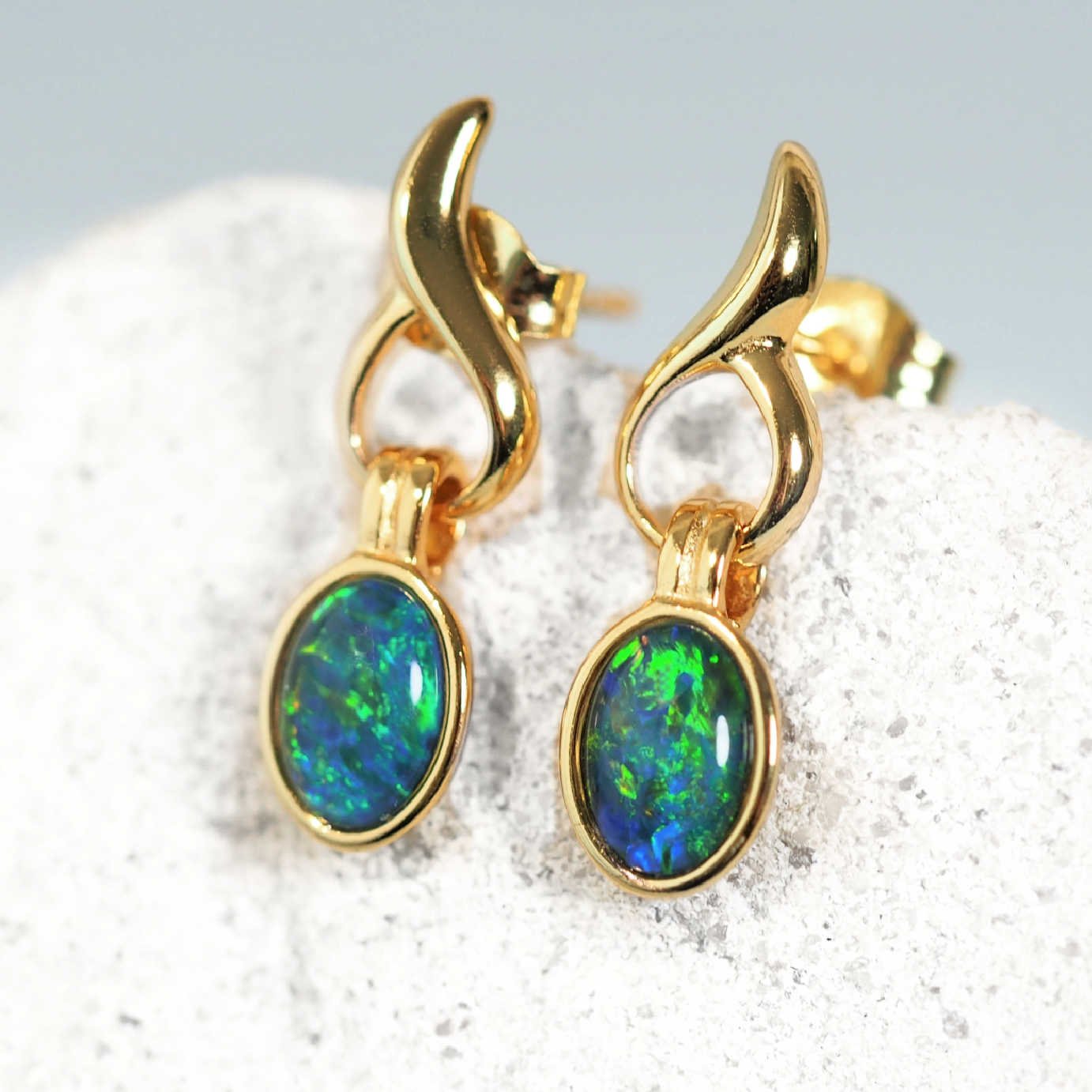 Gold earrings with green opal stones on a textured surface