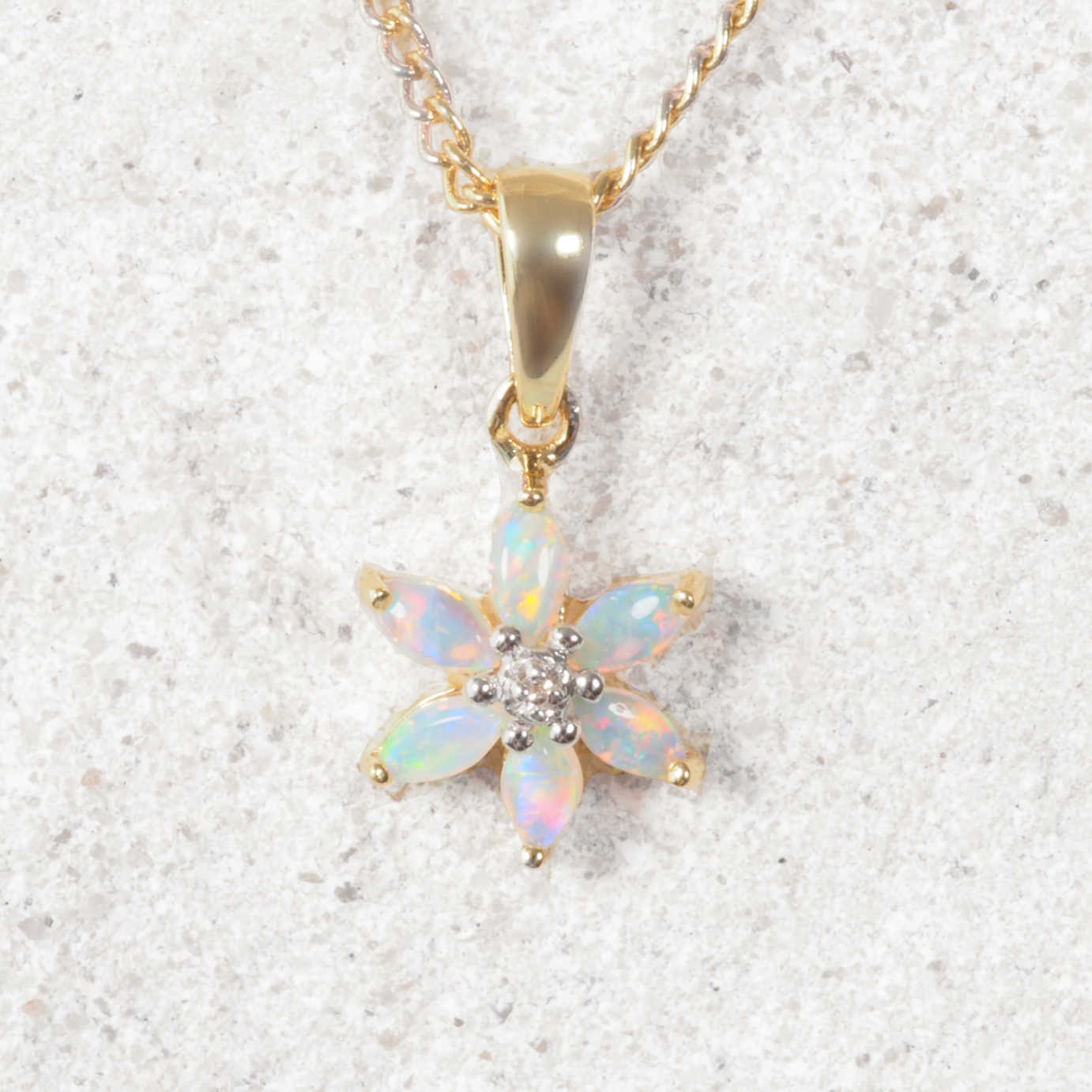 Opal flower pendant with diamond center on a gold chain against a white background