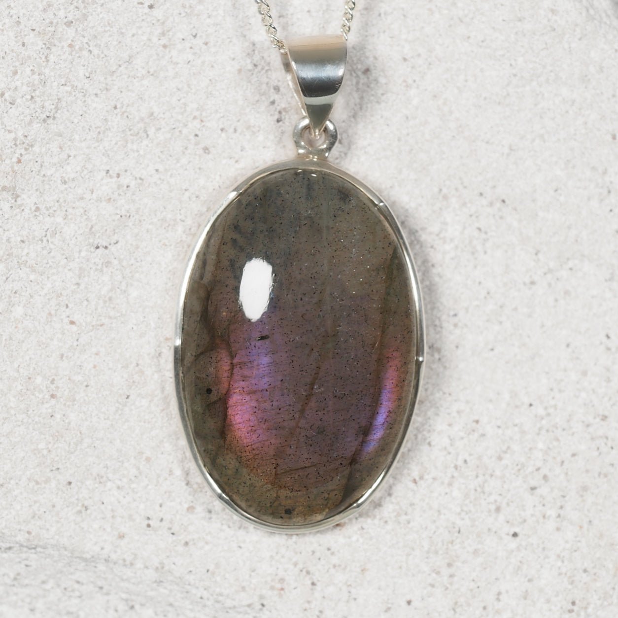 Labradorite pendant on a silver chain against a textured white background