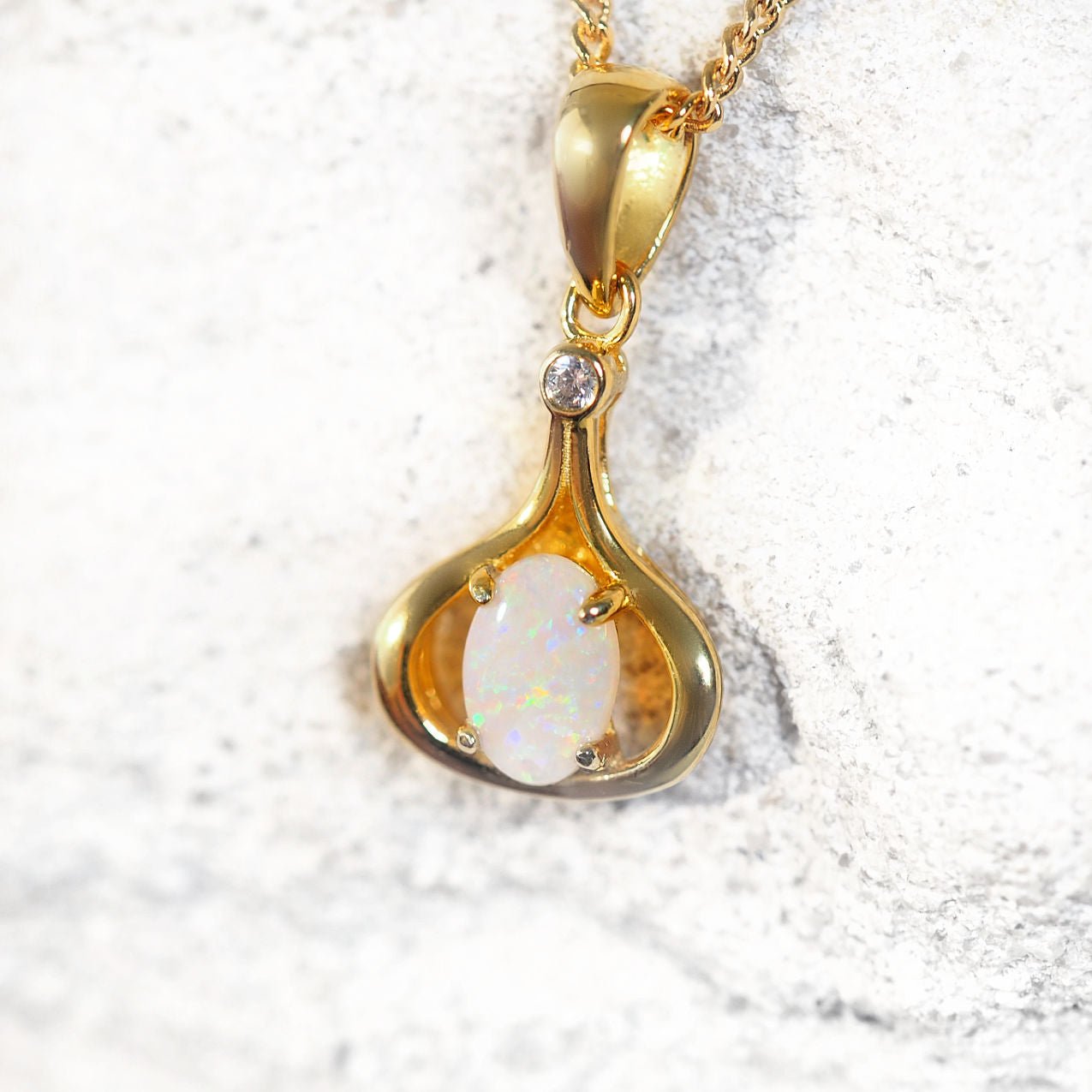 Gold pendant with opal stone on a textured white background