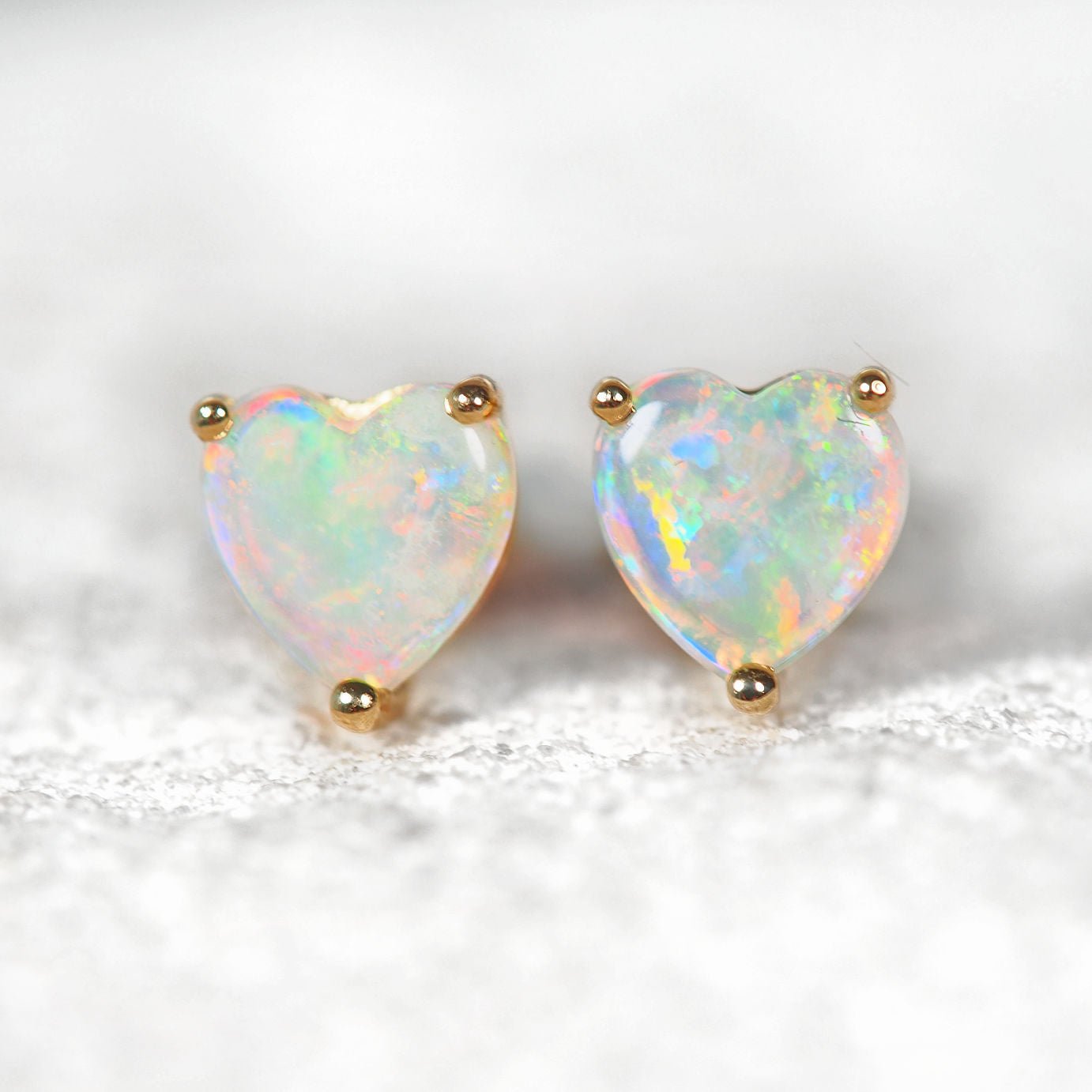 Heart-shaped opal earrings with gold posts on a white background