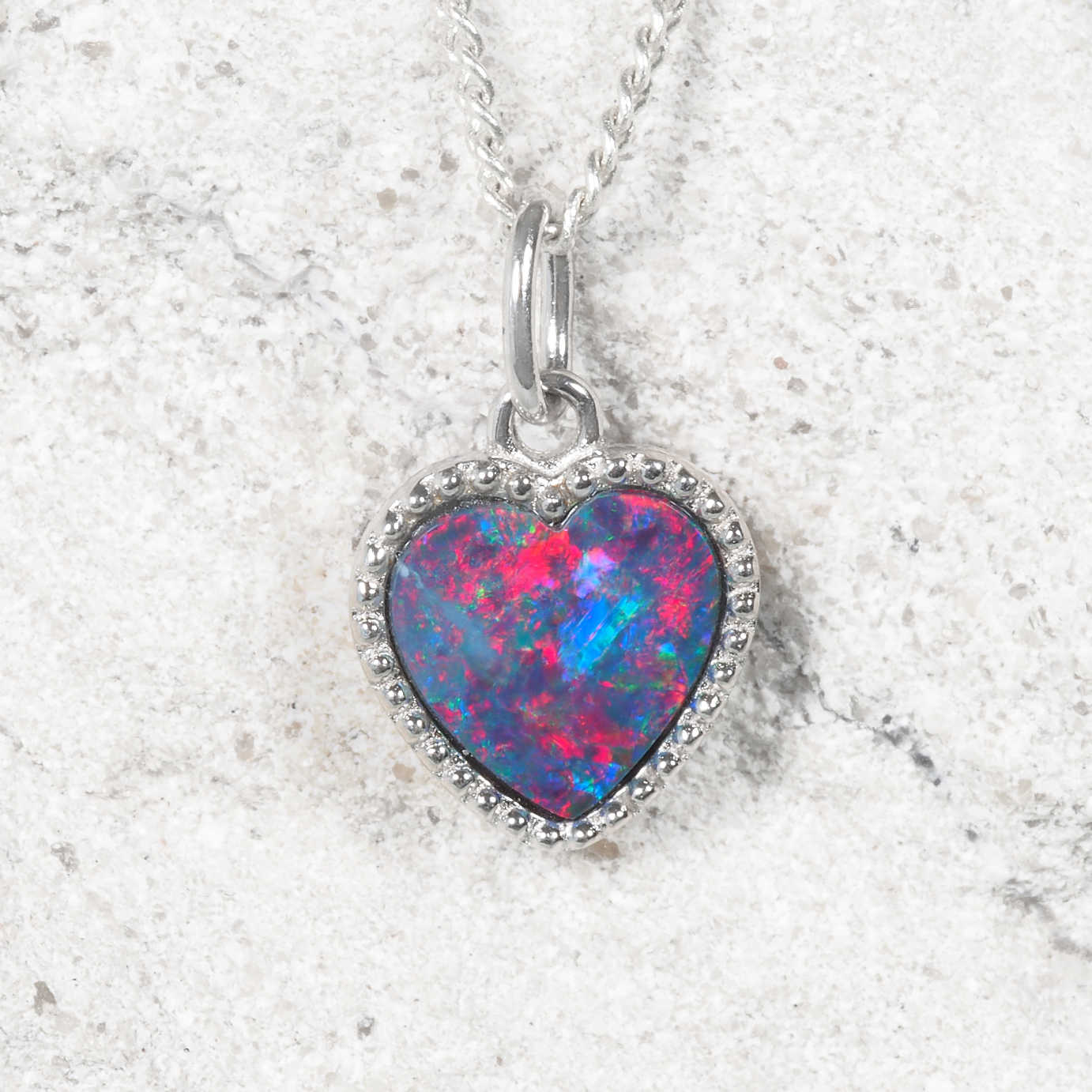 Heart-shaped opal pendant on a silver chain against a light gray background