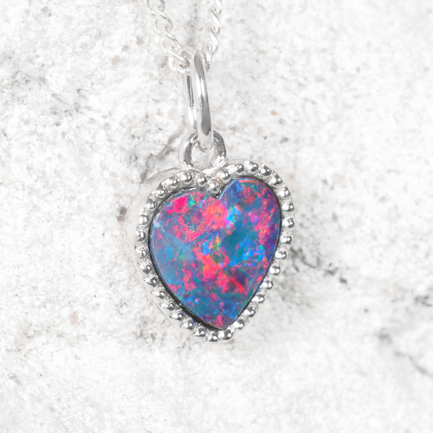 Heart-shaped silver Australian opal pendant on a silver chain against a light gray background